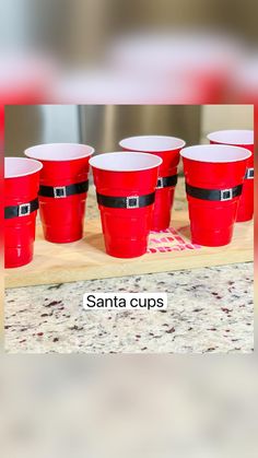 six red cups sitting on top of a wooden tray with santa's belt around them