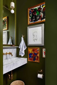 a bathroom with green walls and pictures on the wall above the sink, along with a wicker basket