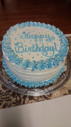 a birthday cake with blue frosting on a glass platter sitting on a table