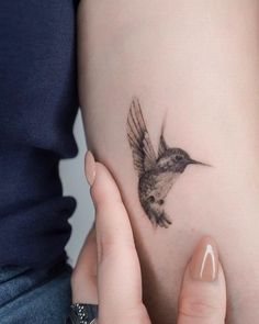 a woman's arm with a small bird tattoo on the left side of her body