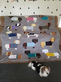 a dog laying on the floor in front of a couch covered with a blanket made to look like dogs