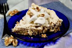 a blue plate topped with a piece of cake covered in whipped cream and walnuts