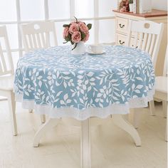 a blue table cloth with white flowers on it and a vase of pink roses in the center