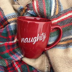 a red coffee mug with the word naught on it sitting on a plaid blanket