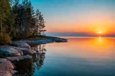 the sun is setting over the water and some trees are in the foreground with rocks on either side