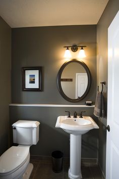 a white toilet sitting next to a sink in a bathroom under a round mirror on the wall