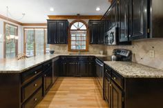 a large kitchen with black cabinets and wood flooring, along with a window that looks out onto the yard