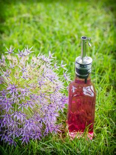 a bottle of liquid sitting on top of a lush green field next to a purple flower