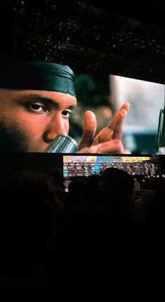 a man holding a cell phone to his mouth while standing in front of a large screen