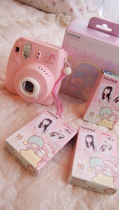 a pink camera sitting on top of a bed next to two boxes with stickers