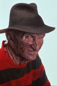 an old man wearing a black hat and striped shirt with blood on his face,