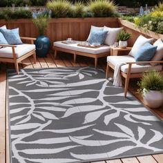 an outdoor area rug with chairs and pillows on it, in front of a wooden deck