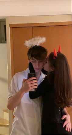 two people dressed up as devil and demon kiss each other's forehead while standing in front of a door