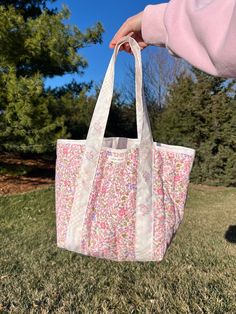 a person holding a pink and white bag in their hand on the grass with trees in the background