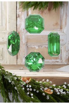 three green jeweled ornaments hanging from a christmas tree with berries and greenery in the foreground