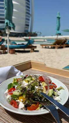 a white plate topped with salad on top of a wooden table next to the beach