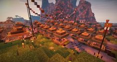 a large group of buildings and flags in a minecraft village with mountains behind them