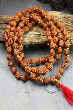 This simple hand-crafted mala featuring a deep red tassel, is made of 108 knotted Rudraksha seed beads and is perfect for your everyday ritual and mediation. Legend has it that the first Rudraksha seeds were created from tears of Lord Shiva as they fell on the earth and formed into a tree. Rudraksha seeds have wonderful spiritual and medicinal properties and, you can feel their power as you count through the beads one by one to recite your chosen mantra or intention. The number 108 holds spiritu Spiritual Wooden Beads Mala For Meditation, Hand-strung Spiritual Mala For Meditation, Spiritual Hand-strung Mala For Meditation, 108 Spiritual Beads For Meditation, 108 Spiritual Meditation Beads, Bohemian Mala With 108 Beads For Meditation, Holistic Wooden Beads Mala For Rituals, Holistic Mala With 108 Beads For Meditation, Holistic Wooden Mala For Rituals