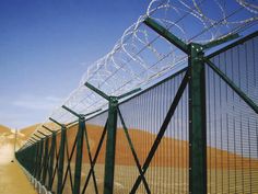 a fence with barbed wire on top and dirt road in the background, along side sand dunes