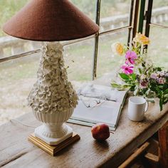 a white vase sitting on top of a wooden table next to a cup and book