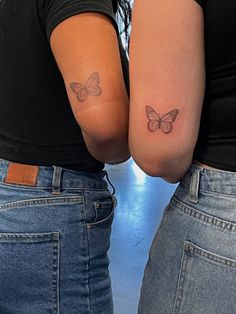 two women with butterfly tattoos on their arms, both holding each other's hands