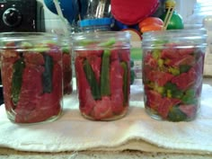 three jars filled with pickles and other vegetables