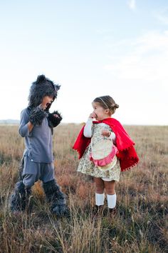 two children dressed up in costumes walking through a field with one child wearing a cat costume and the other holding a stuffed animal