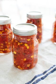 four jars filled with pickles sitting on top of a white cloth covered tablecloth