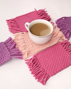 a cup of coffee sitting on top of a table next to some knitted placemats