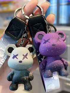 two keychains with different designs on them in the shape of bears, one is purple and one is black