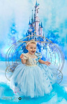 a baby girl in a blue dress is smiling at the camera with a castle behind her