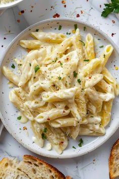 a white plate topped with pasta next to two slices of bread on top of a table