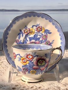 a cup and saucer sitting on top of a sandy beach next to the ocean