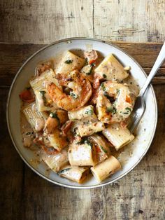 a white bowl filled with pasta and shrimp on top of a wooden table next to a fork