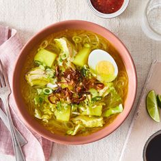 a pink bowl filled with soup next to two spoons and an egg on top