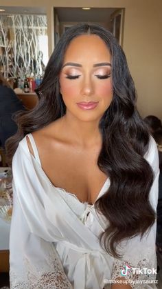 a woman with long dark hair wearing a white dress and posing for the camera in front of a table