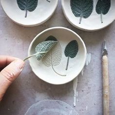 three white bowls with green leaf designs on them, one being held by a person's hand