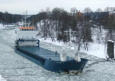 a large blue boat floating on top of ice covered water next to trees and snow covered ground