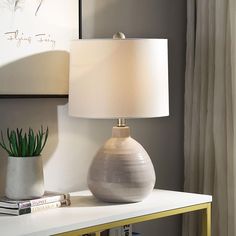 a table with a lamp on it next to a book shelf and a plant in a vase