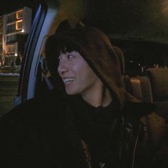 a young man sitting in the passenger seat of a car at night wearing a hoodie