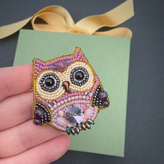 a hand holding an owl brooch with beading on it's face and eyes