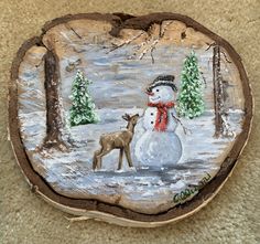 a snowman and deer painted on a piece of wood with trees in the background