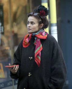 a woman is walking down the street looking at her cell phone and wearing a scarf