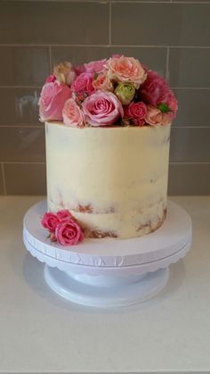 a white cake with pink flowers on top sitting on a counter next to a tiled wall