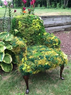 a chair made out of moss sitting in the grass next to some flowers and plants