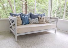 a couch with pillows on it sitting in front of a window overlooking the woods and trees