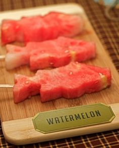 some food is sitting on a cutting board with toothpicks in it and watermelon sticks sticking out of them