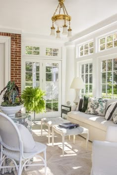 a living room filled with white furniture and lots of windows covered in plants on either side of the couch