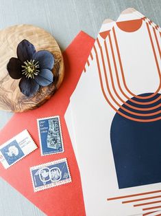 an envelope with stamps and a flower sitting on top of it next to a wooden plate