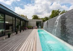 an outdoor swimming pool with wooden decking and water feature on the side of it